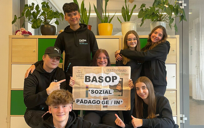 Schüler*innen halten ein Schild mit der Aufschrift "BASOP Sozialpädagoge/in" in der Hand und lächeln in die Kamera, um die neue Ausbildung zu bewerben.