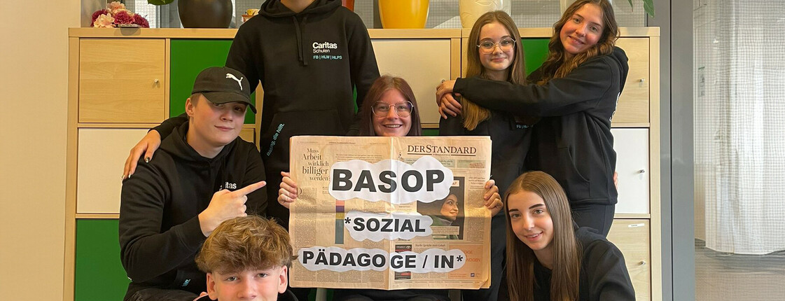 Schüler*innen halten ein Schild mit der Aufschrift "BASOP Sozialpädagoge/in" in der Hand und lächeln in die Kamera, um die neue Ausbildung zu bewerben.