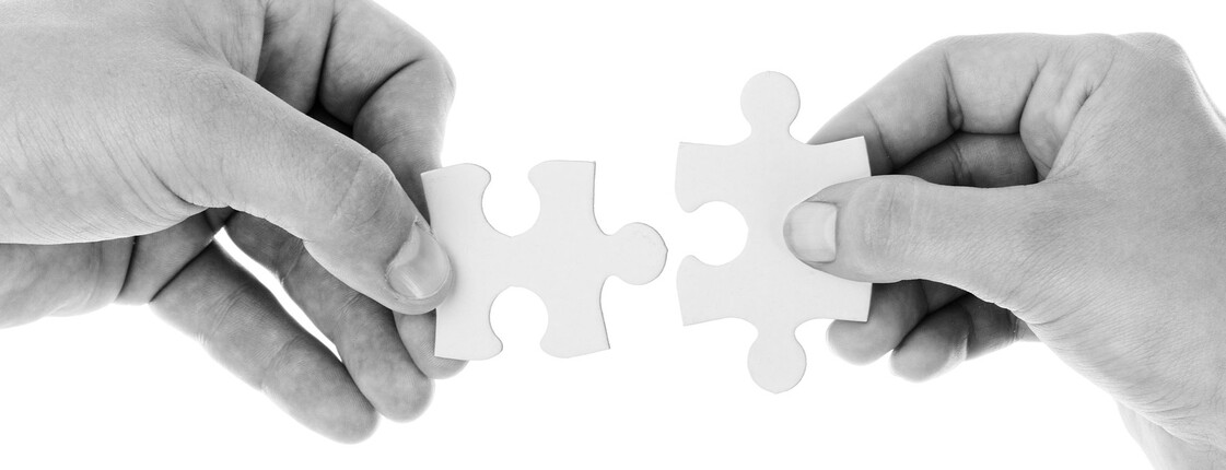 Zwei Hände halten jeweils ein Puzzlestück, die sich einander annähern.