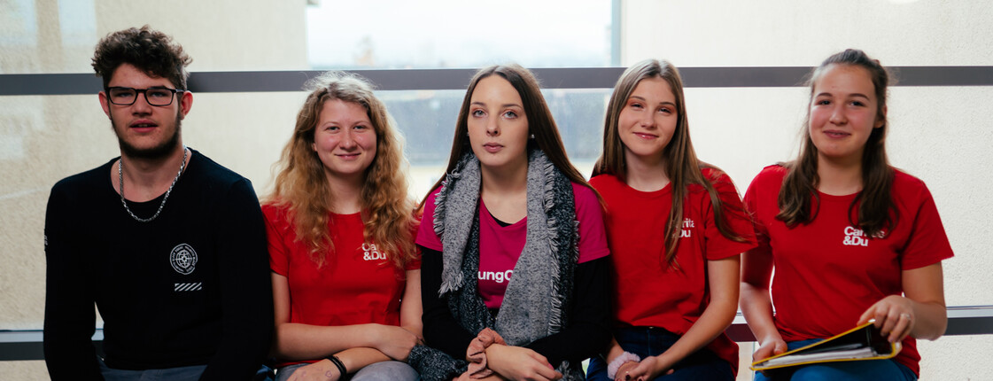 Ein Schüler und vier Schülerinnen sitzen auf einer Bank des Schulgebäudes.