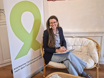 Elena Bucher, Absolventin des Caritas Lehrgangs Ehe- Familien- und Lebensberatung sitzt auf einer weißen Couch vor einem Rollup der "Aktion Leben".