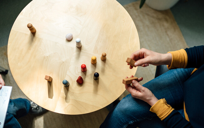 Ein Tisch in der Vogelperspektive, zwei Menschen sitzen sich gegenüber und Spielfiguren stehen auf dem Tisch.