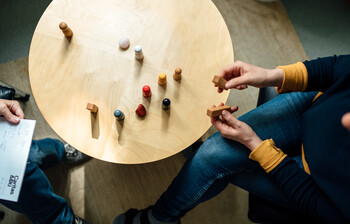 Ein Tisch in der Vogelperspektive, zwei Menschen sitzen sich gegenüber und Spielfiguren stehen auf dem Tisch.
