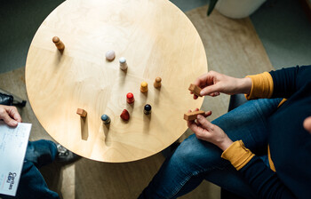 Ein Tisch in der Vogelperspektive, zwei Menschen sitzen sich gegenüber und Spielfiguren stehen auf dem Tisch.