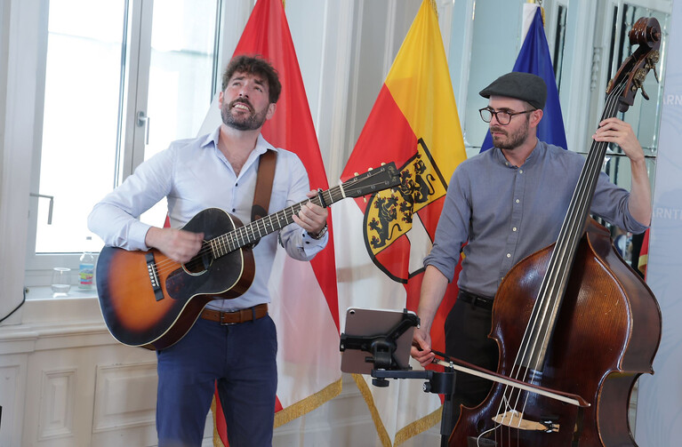 Musiker mit Gitarre und Kontrabass spielen vor Fahnen des Landes Kärnten und Österreich