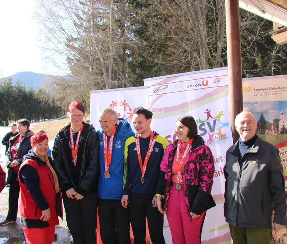 Athlet*innen mit Medaillen stehen vor Bannern des Wintersporttags im Freien