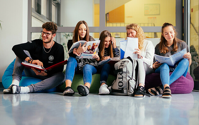 Ein Schüler und fünf Schüler*innen sitzen auf Sitzsäcken im Gand der Schule und lernen miteinander.