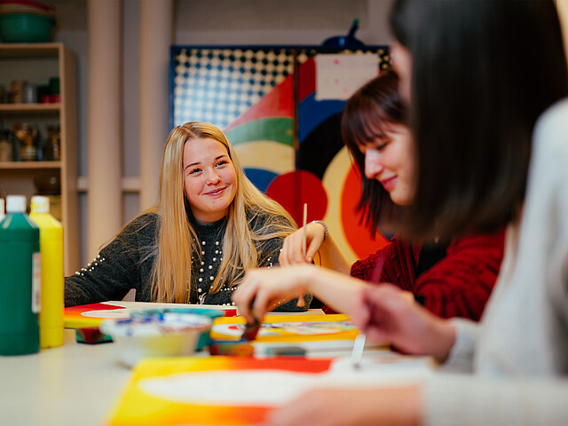 Schülerinnen unterhalten sich im Kreativunterricht miteinander und malen.