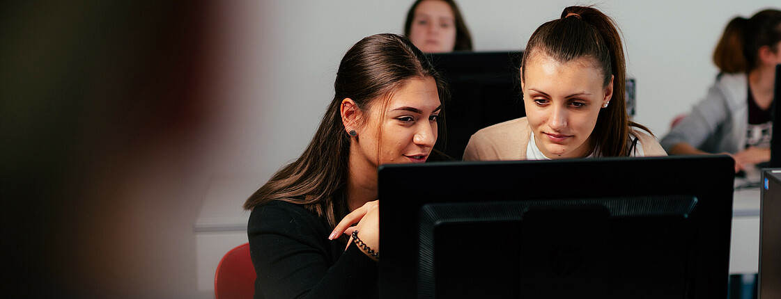 Zwei Schülerinnen sehen sich gemeinsam etwas am Computer-Bildschirm an.