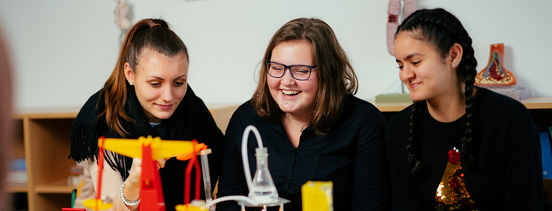 Drei Schülerinnen sitzen vor einem chemischen Experiment.