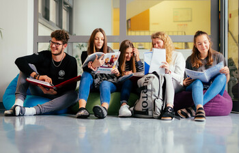 Ein Schüler und fünf Schüler*innen sitzen auf Sitzsäcken im Gand der Schule und lernen miteinander.