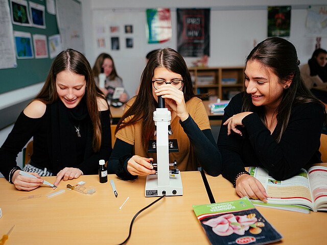 Drei Schülerinnen beim naturwissenschaftlichen Unterricht an einem Mikroskop.